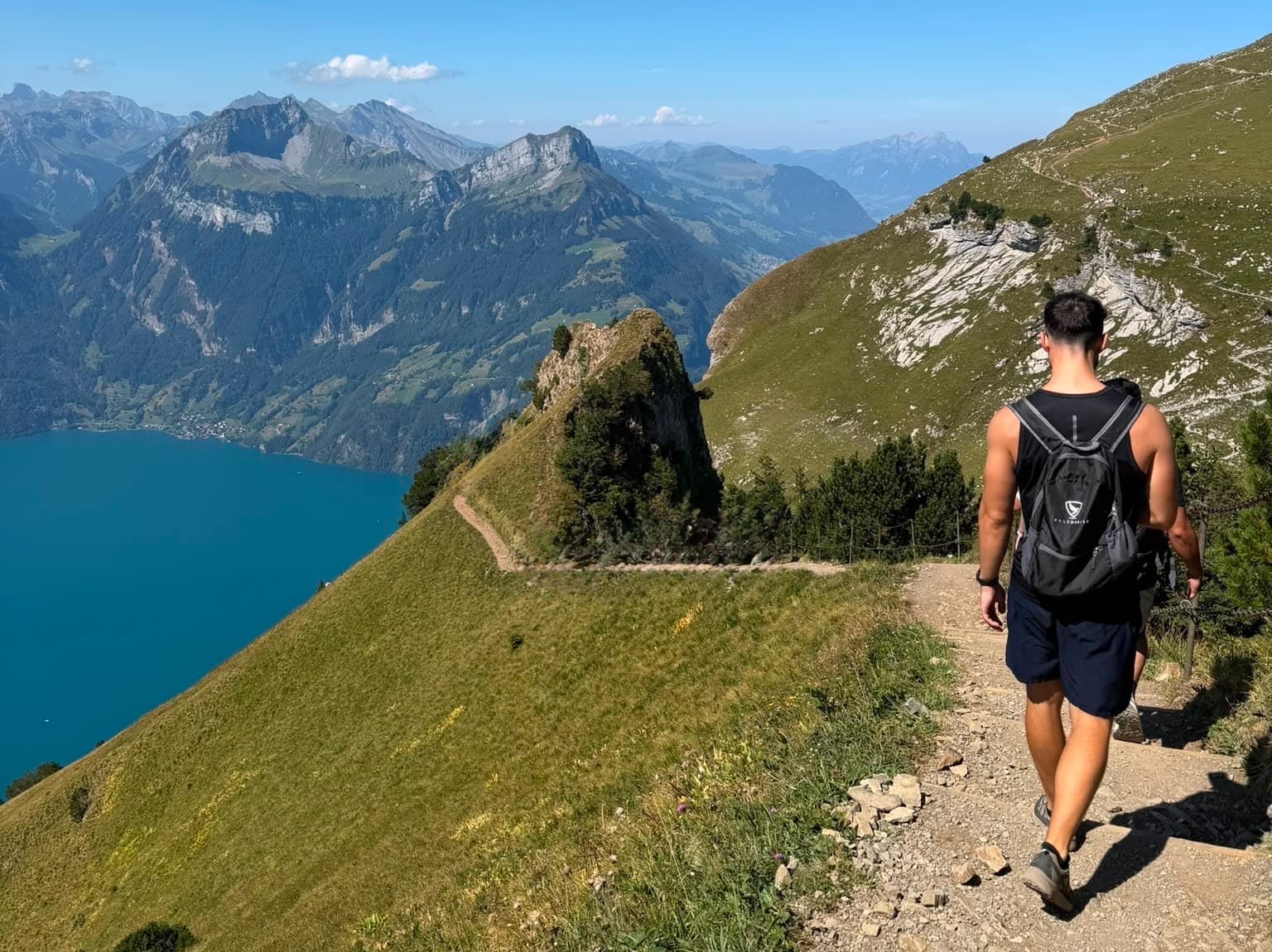 Me walking down a mountain path above a lake, backpack on.