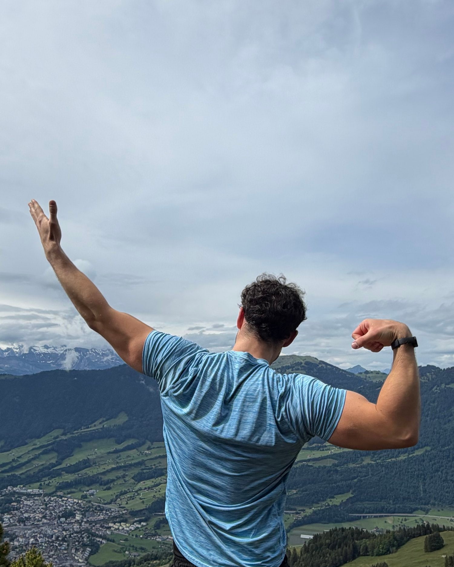 Cezar on a rocky peak above an alpine valley, one arm raised, one flexed.